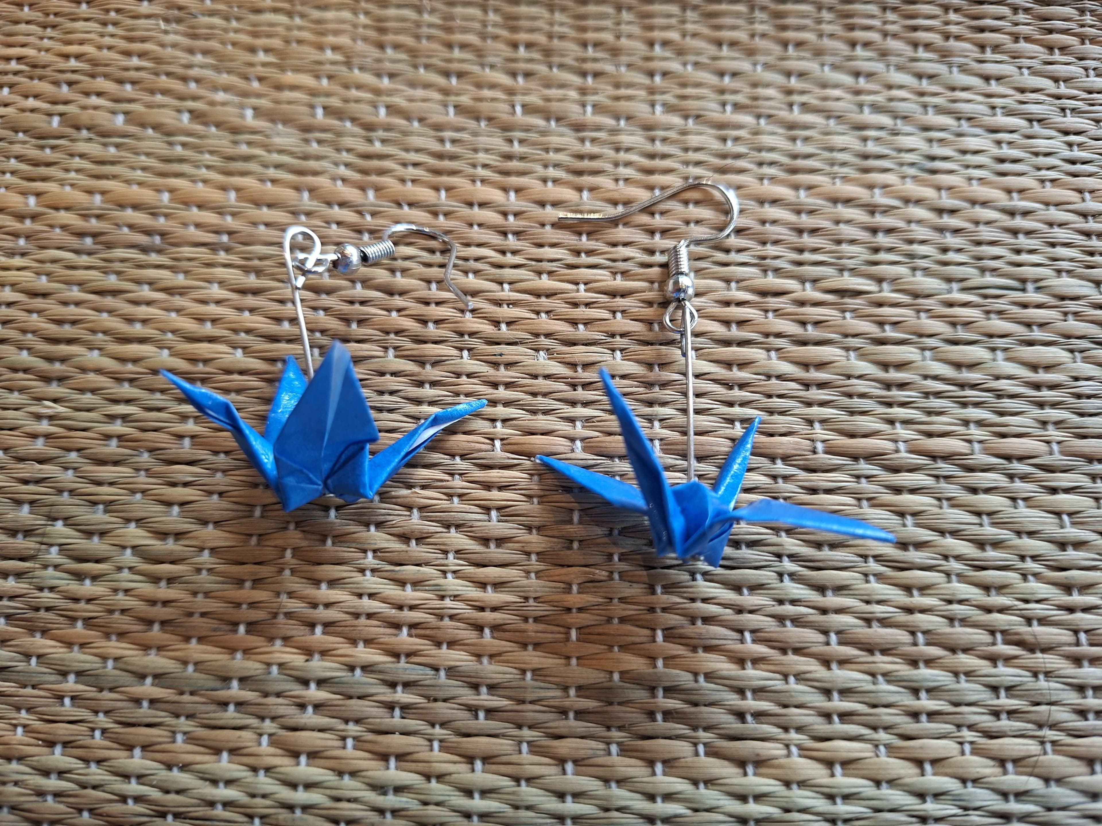 Blue origami crane earrings on a woven background